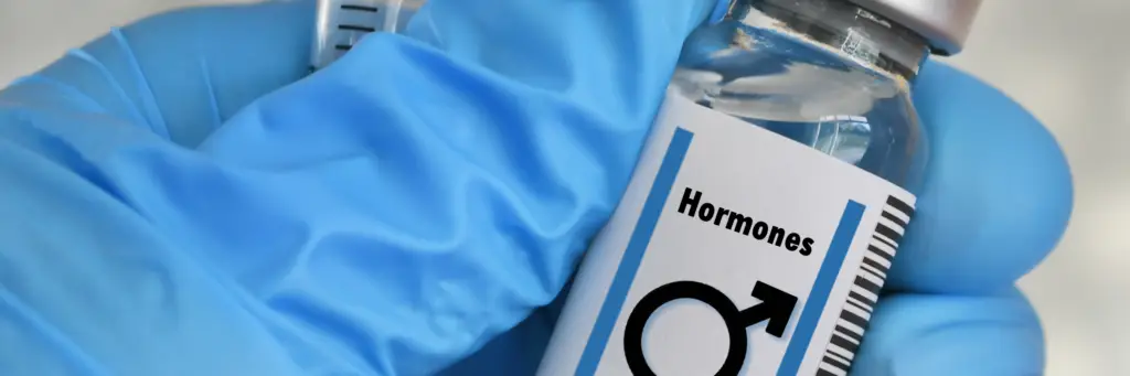 Vial of hormone therapy labeled with male symbol, held in gloved hand, representing hormone replacement therapy for men.