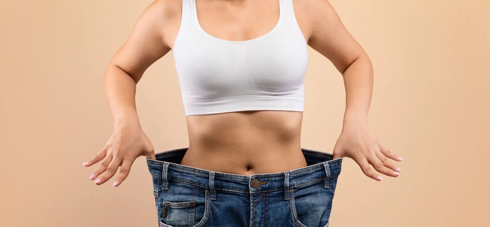 Woman holding oversized jeans, showcasing weight loss success, emphasizing effective weight management solutions with peptides like Semaglutide and Tirzepatide.