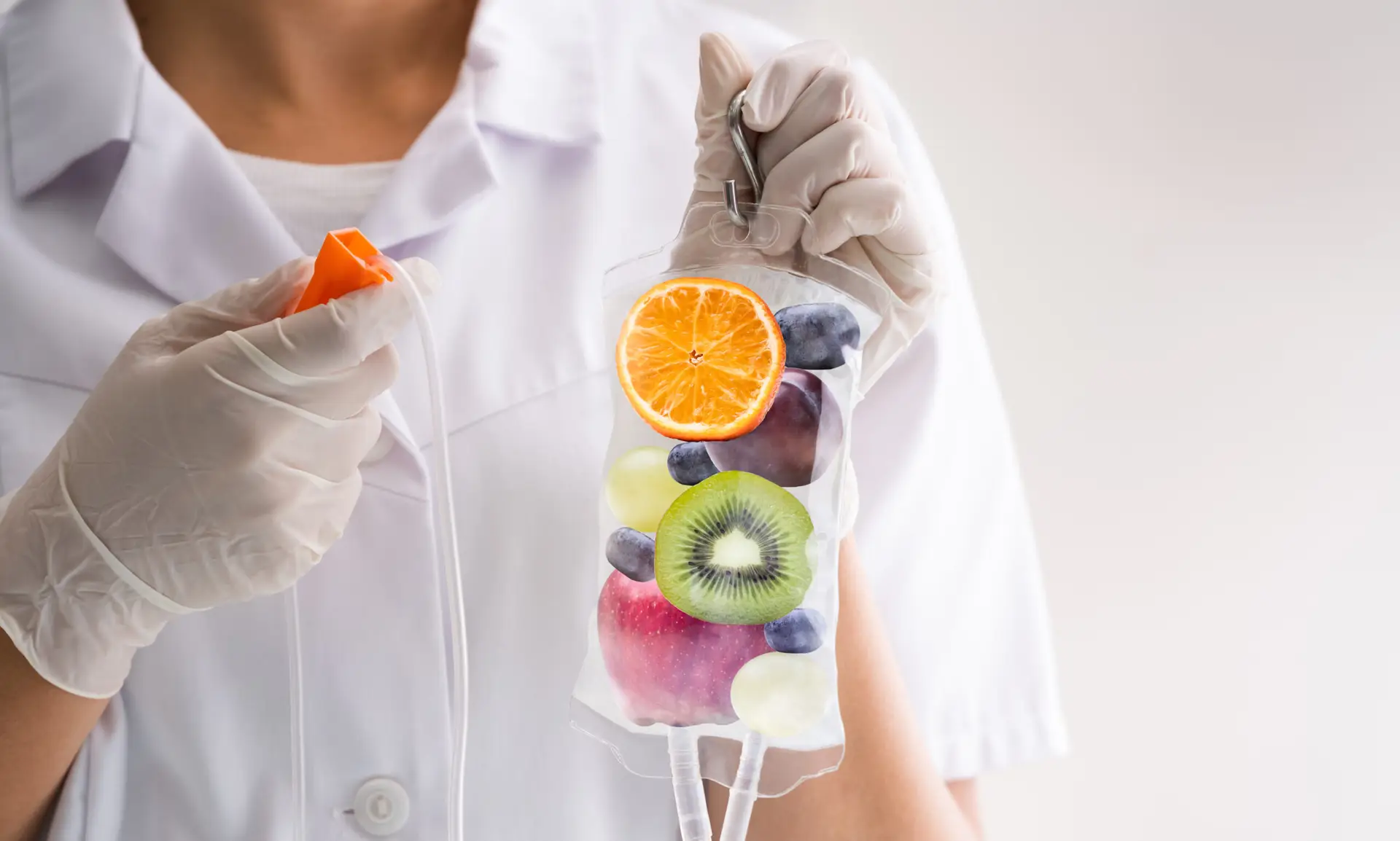 Healthcare professional holding an IV bag filled with fresh fruits like orange, kiwi, apple, and blueberries, representing IV nutrition therapy benefits for health and wellness.