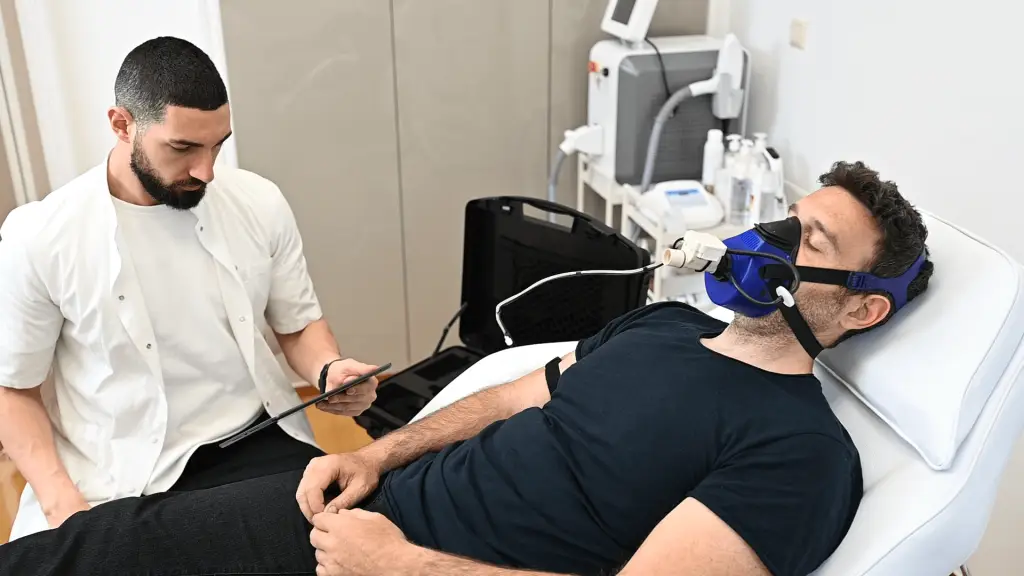 Man undergoing a Resting Metabolic Rate test with advanced breath analysis, while a healthcare professional observes and records data in a clinical setting.